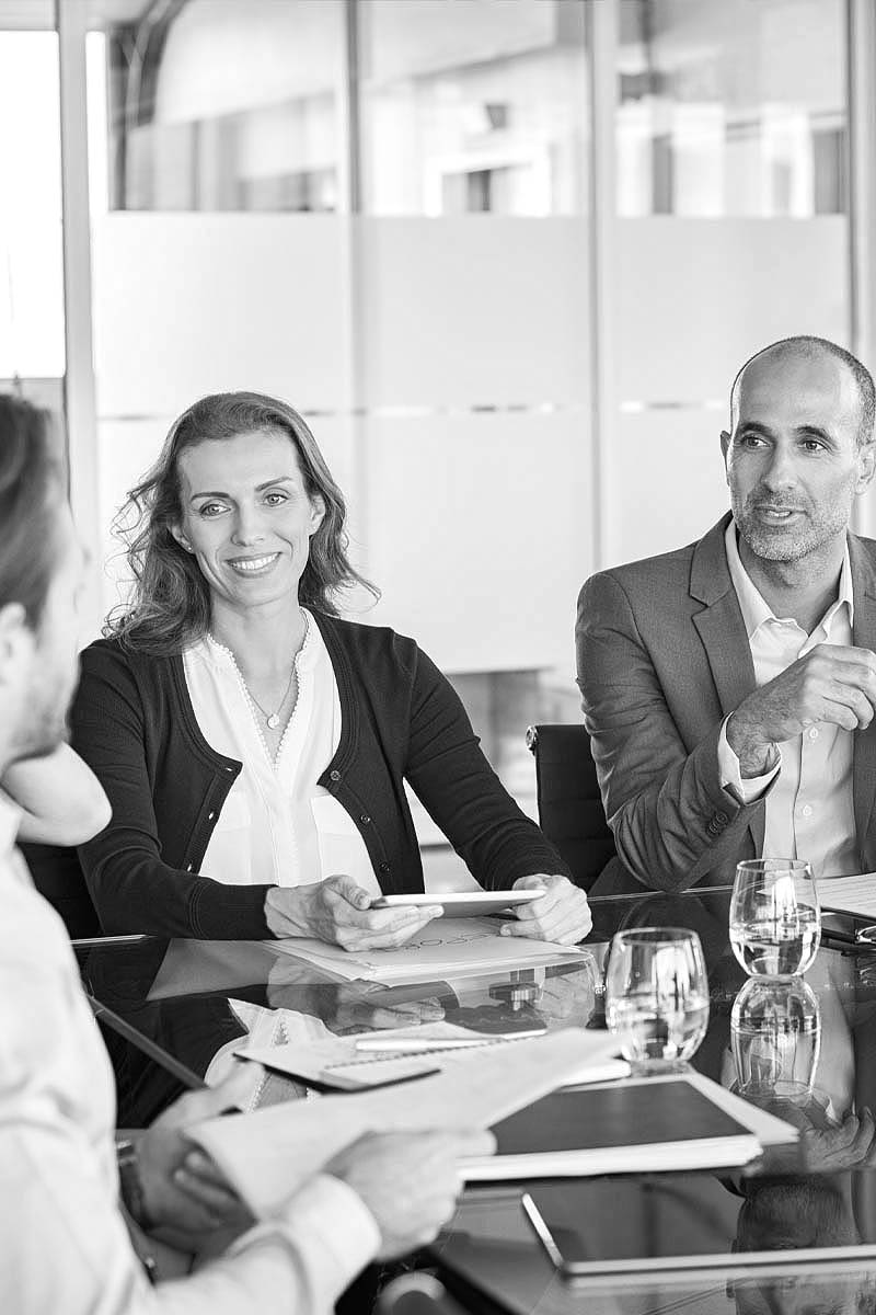 Menschen in Büruraum die an einem Tisch vor einer Scheibe mit Milchglasfolie sitzen.