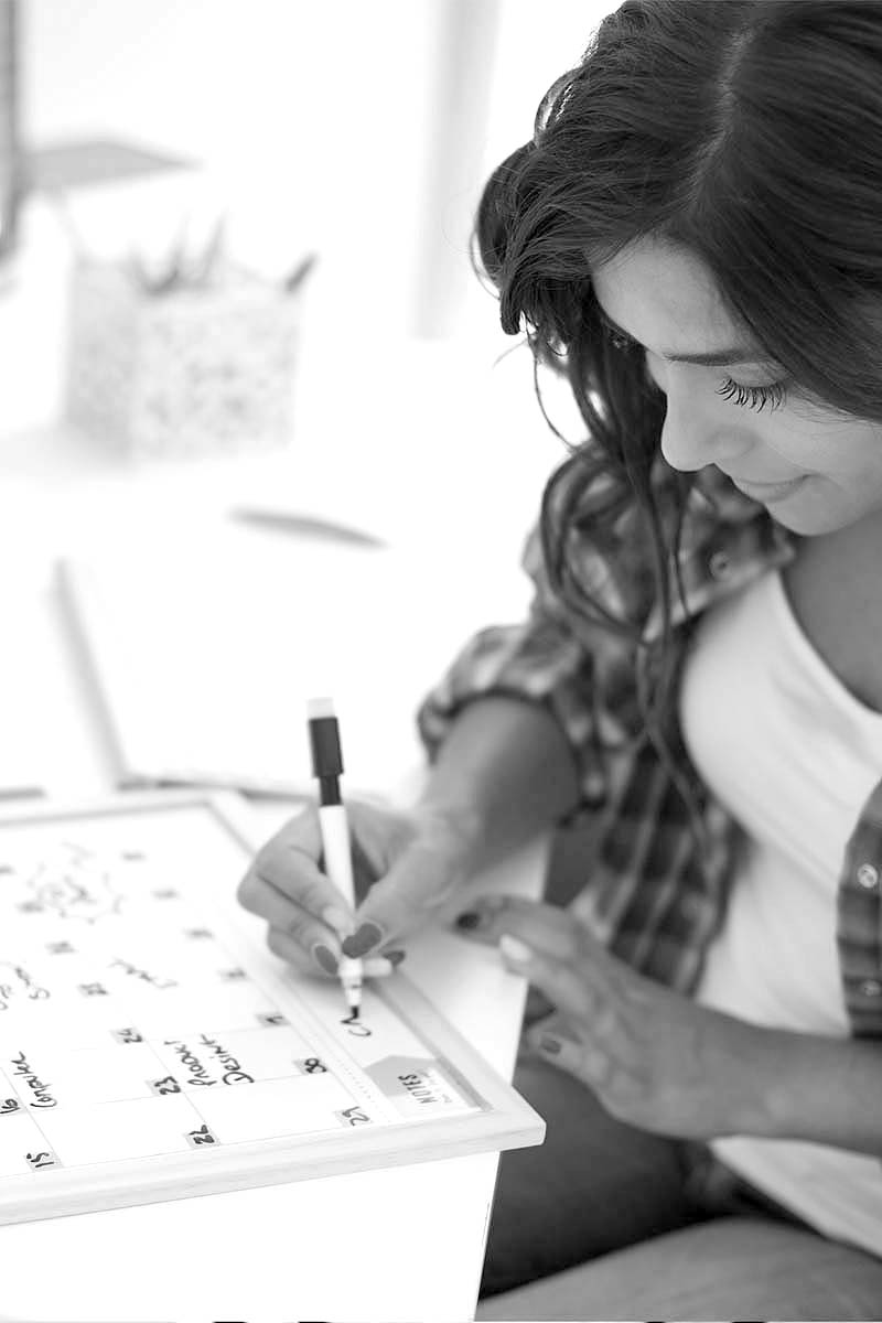 Braunhaarige Frau trägt etwas mit schwarzem Filzstift in ihren Kalender ein.