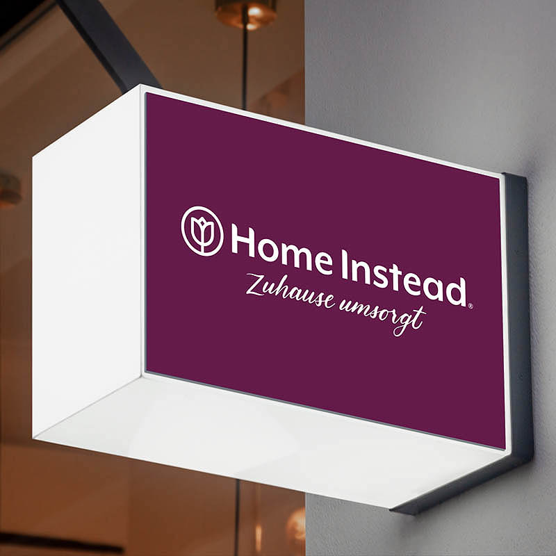 Leuchtschild von Homeinstead an einer Hauswand.