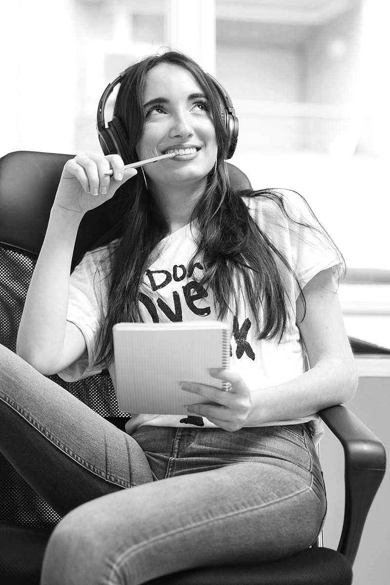 Eine junge Frau sitzt mit Kopfhörern und ihrem Schreibblock auf dem Stuhl.